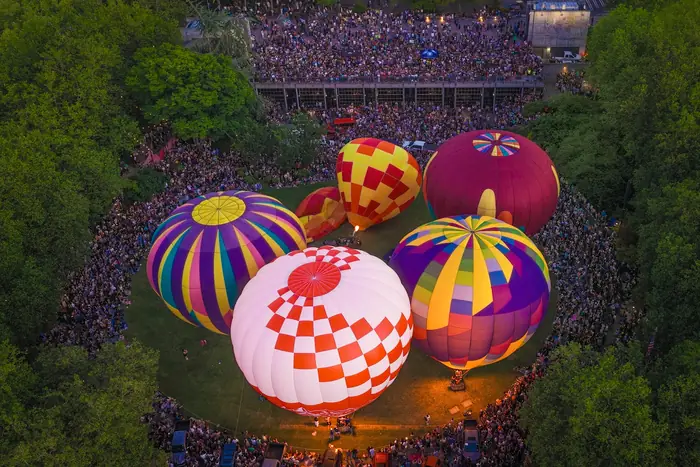 Overhead view of glowing hot air balloons surrounded by a huge crowd at dusk