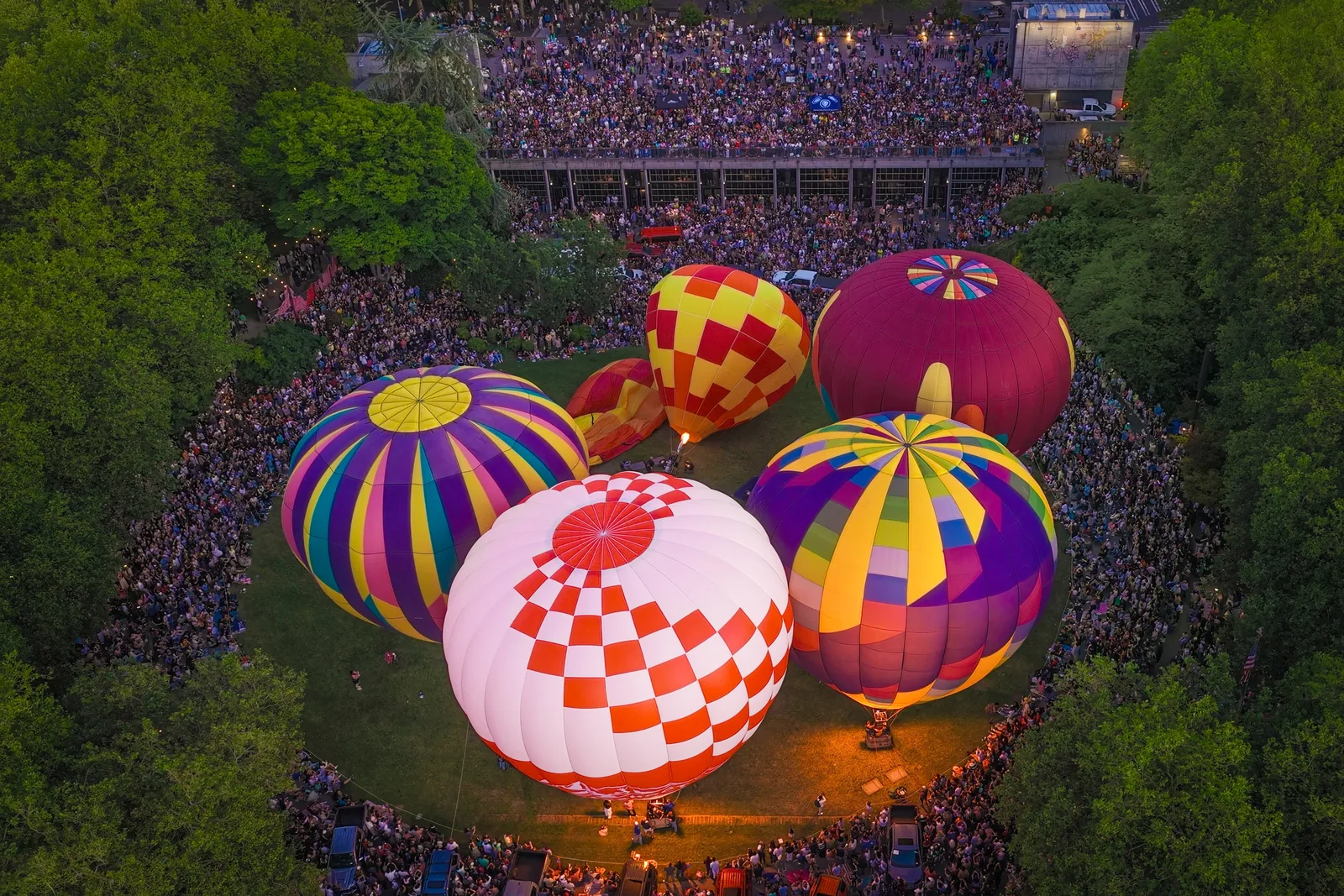 Overhead view of glowing hot air balloons surrounded by a huge crowd at dusk