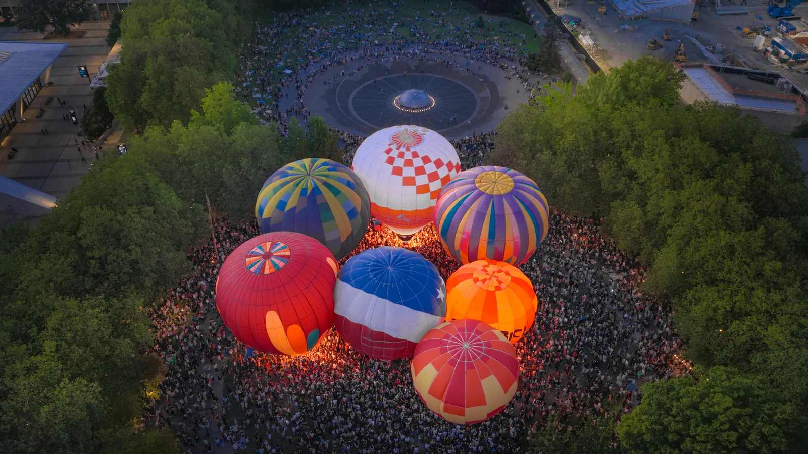 Aerial view of glowing hot air balloons clustered among the trees at Seattle Center at dusk