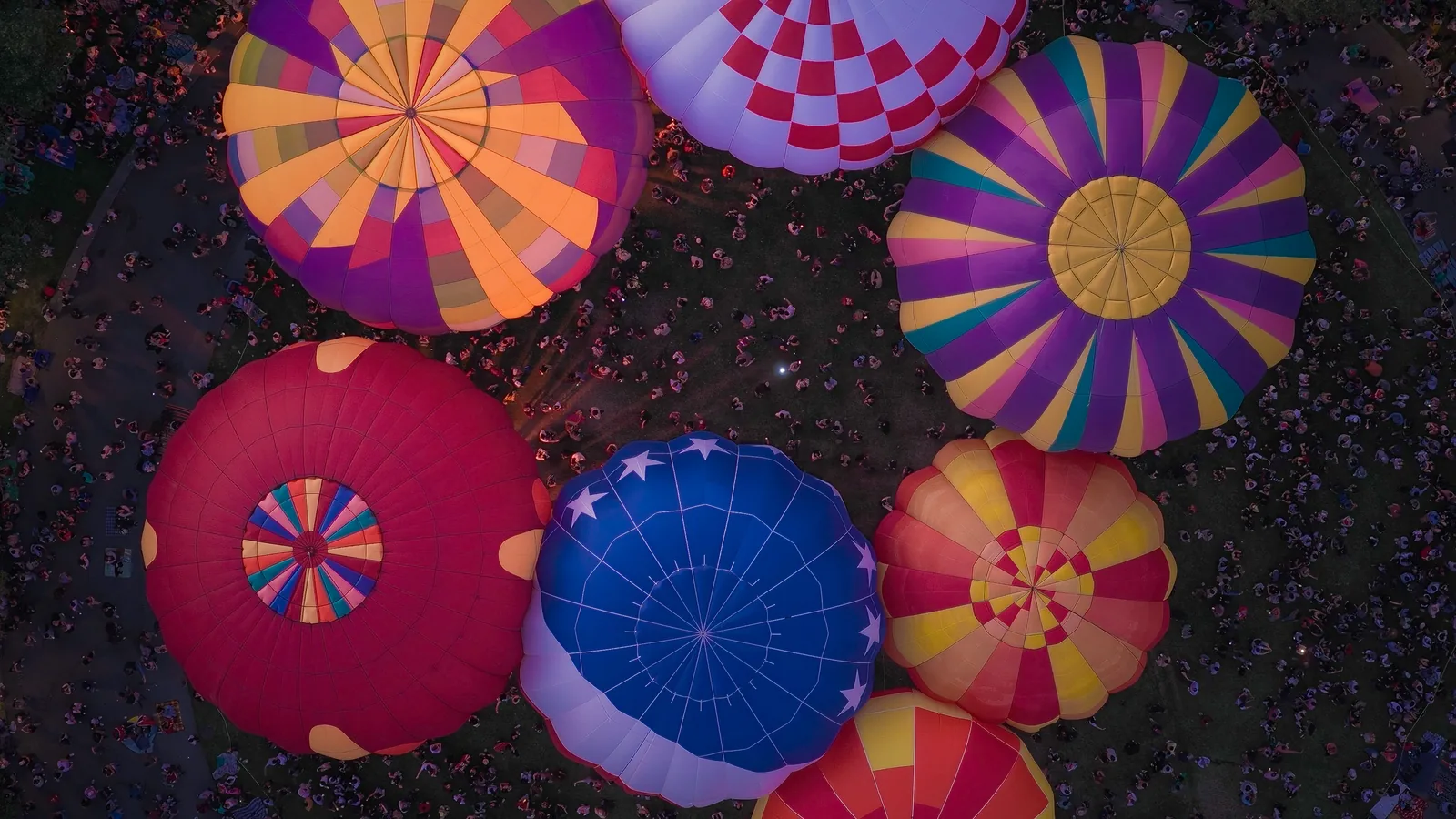 Overhead view of colorful hot air balloon tops ringed by the crowd at night