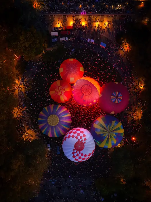 Aerial view of eight glowing hot air balloons ringed by thousands of spectators at night