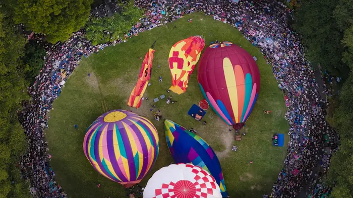 Aerial view of hot air balloons within a ring of thousands of spectators on the lawn