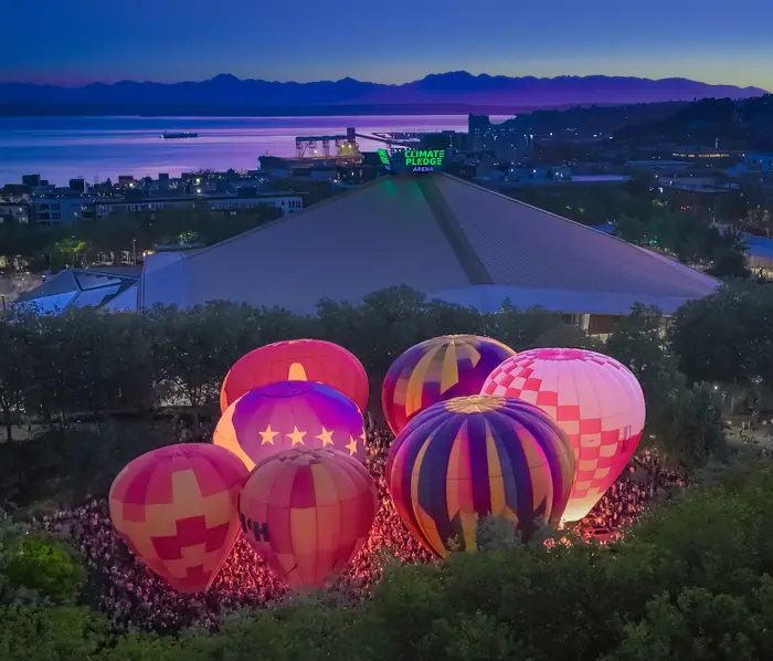Hot air balloons glowing at blue hour with Climate Pledge Arena and Puget Sound beyond