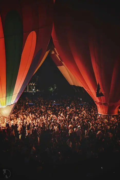 The crowd gathered beneath two towering glowing hot air balloons at night