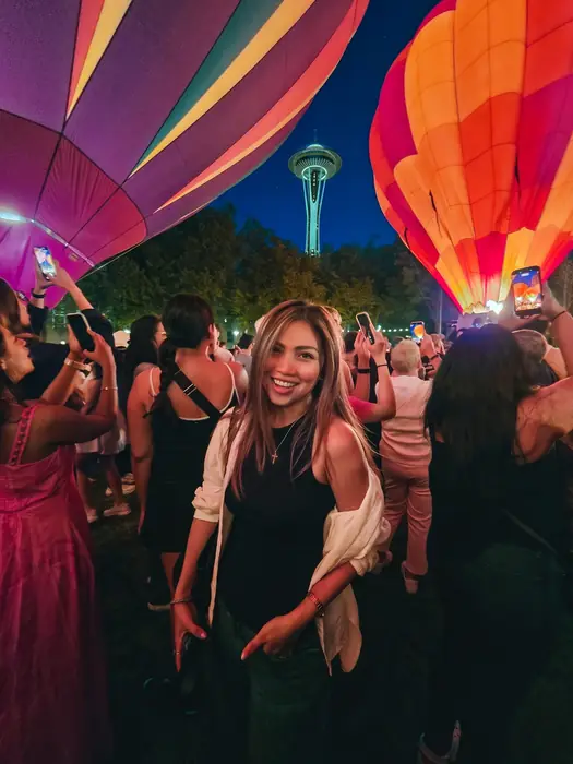 A guest smiles beneath glowing hot air balloons with the Space Needle behind at The Seattle Glow