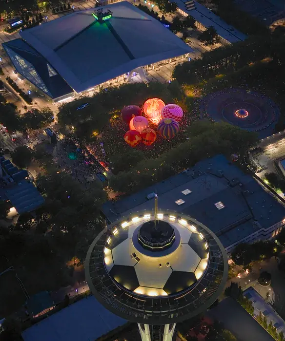 Aerial view past the Space Needle to a cluster of glowing hot air balloons at Seattle Center