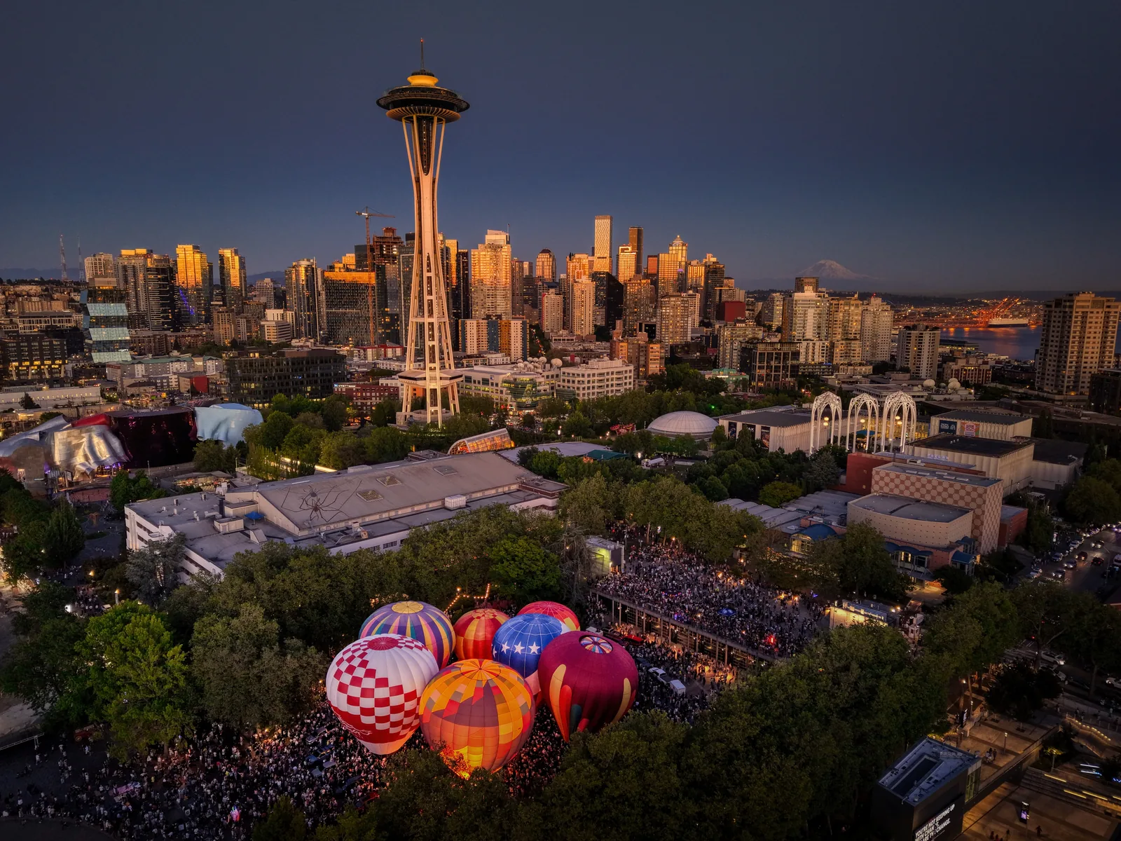 Seattle skyline at golden hour with the Space Needle and Mount Rainier as hot air balloons glow at Seattle Center