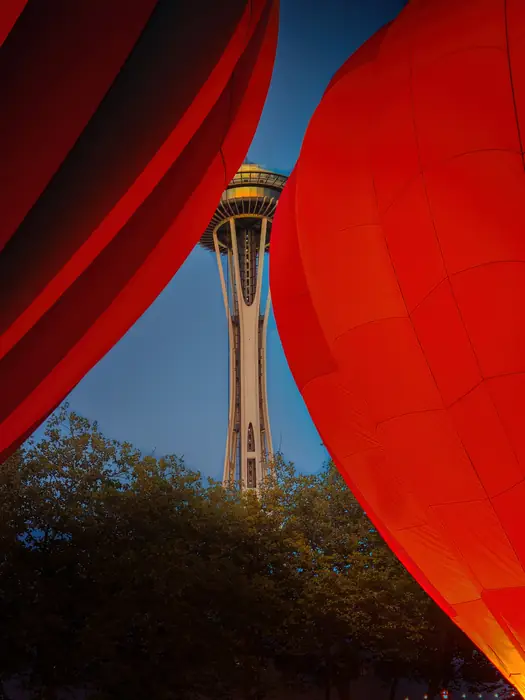 The Space Needle framed between two red hot air balloons at dusk