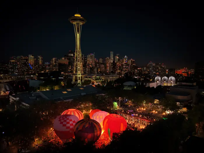 The Space Needle and Seattle skyline at night above glowing hot air balloons at Fisher Pavilion