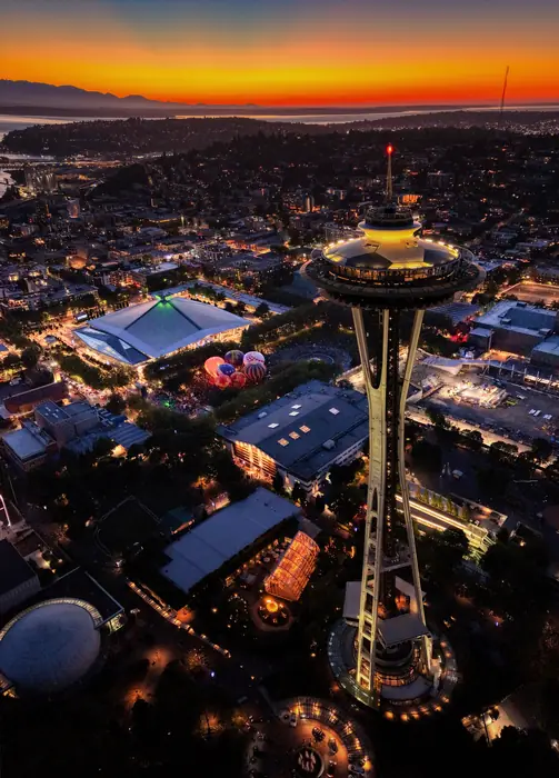 The Space Needle at sunset rising above hot air balloons glowing at Seattle Center