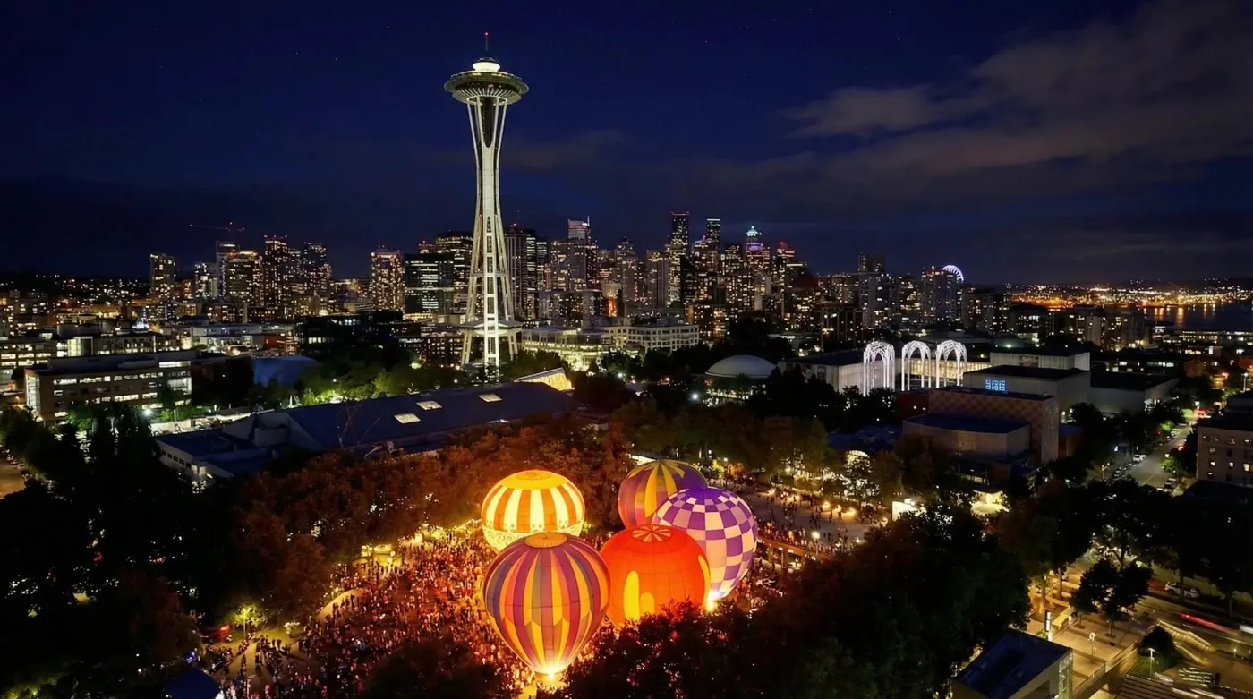 Aerial view of hot air balloons glowing at Seattle Center with the Space Needle and city skyline at night