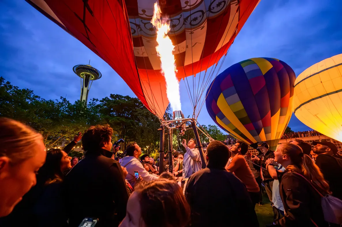 Crowd surrounding hot air balloons firing burners beneath the Space Needle at Seattle Center